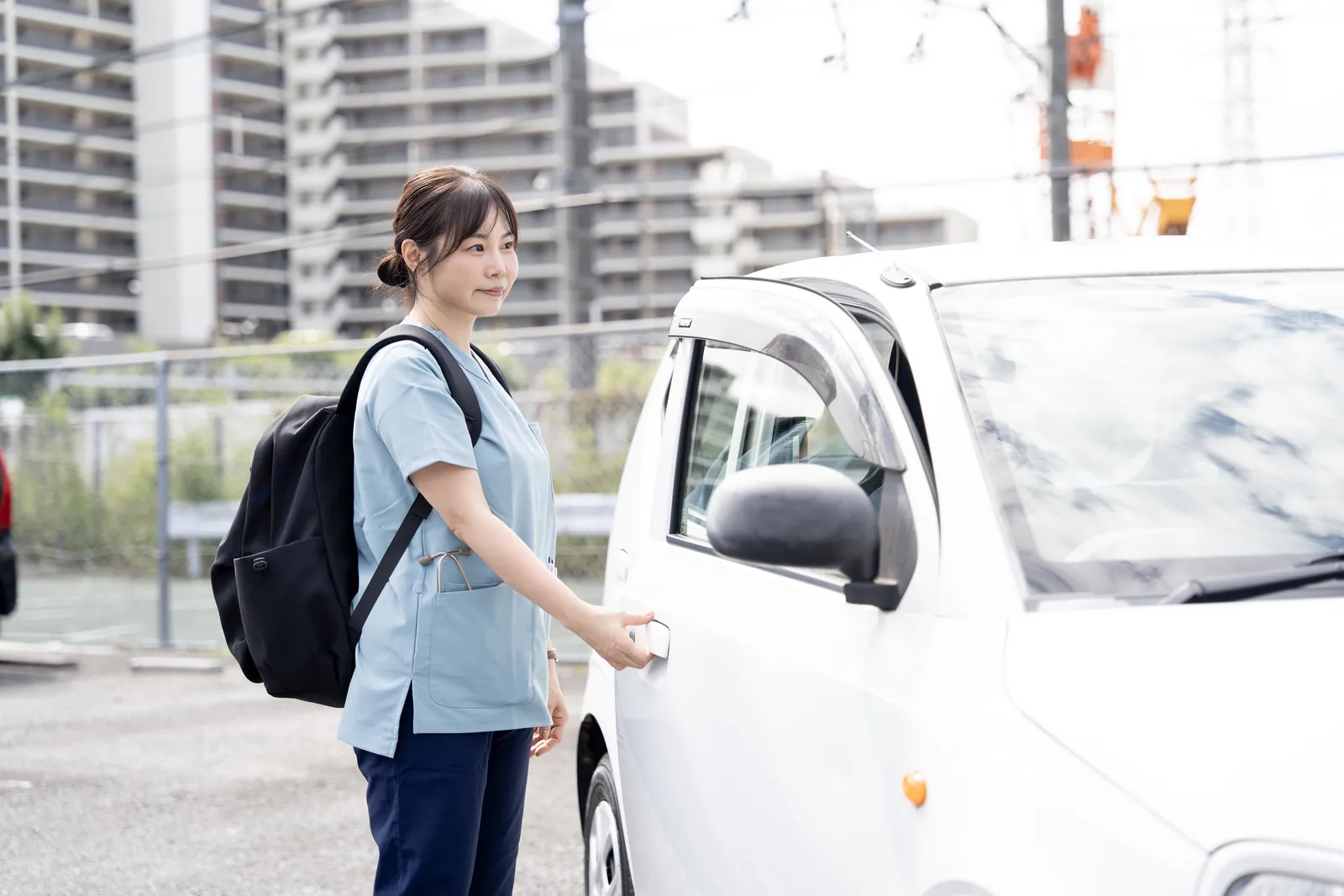 リュックを背負った看護師が、訪問に向かうため社用車に乗り込む様子